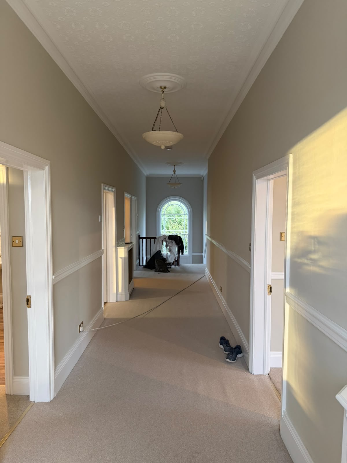 Period landing with neutral walls, white dado rails and door frames, patterned ceiling and an arched window by the stairs