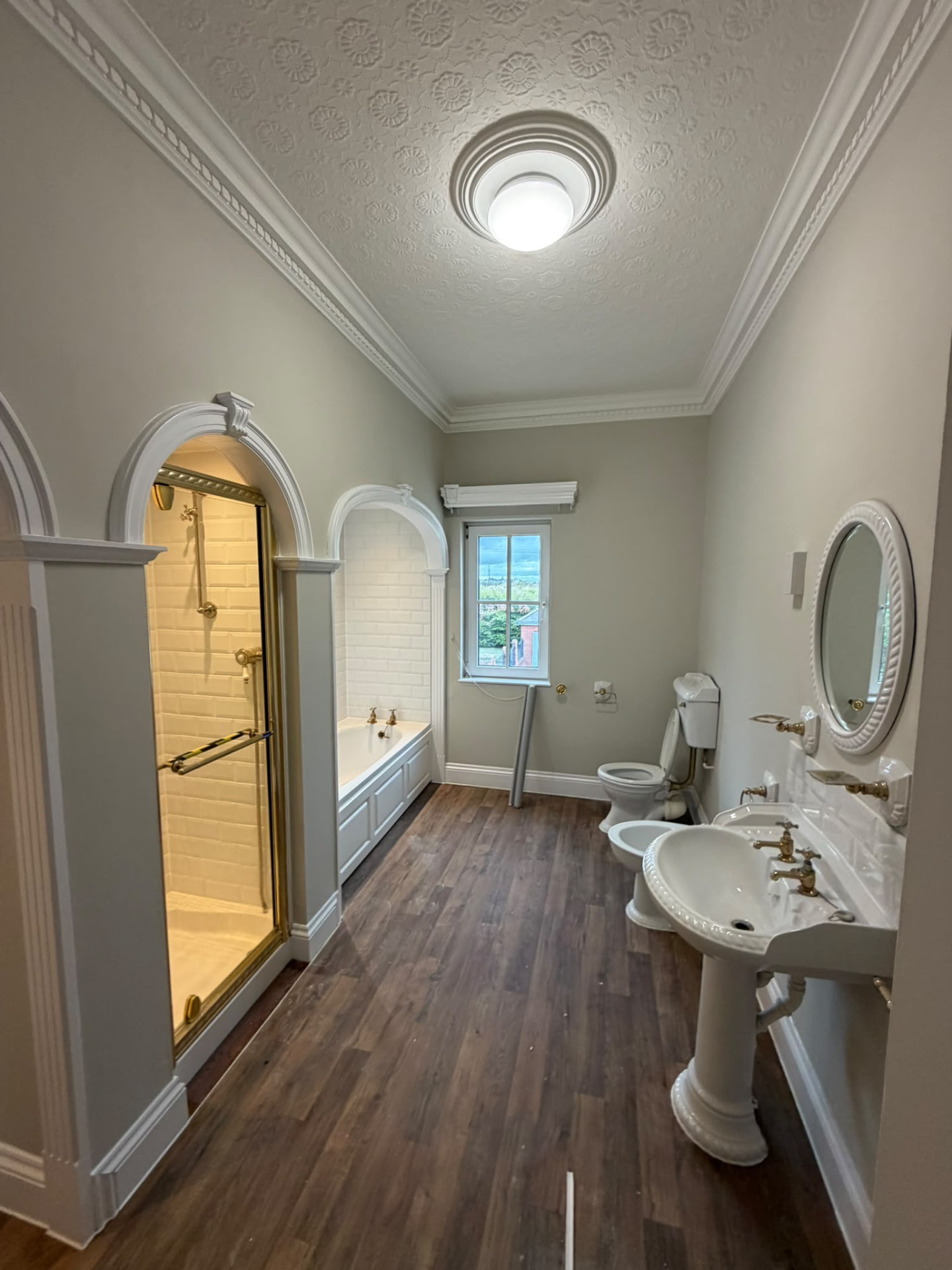 Period bathroom with neutral painted walls, white arched mouldings around the bath and shower, and a patterned ceiling