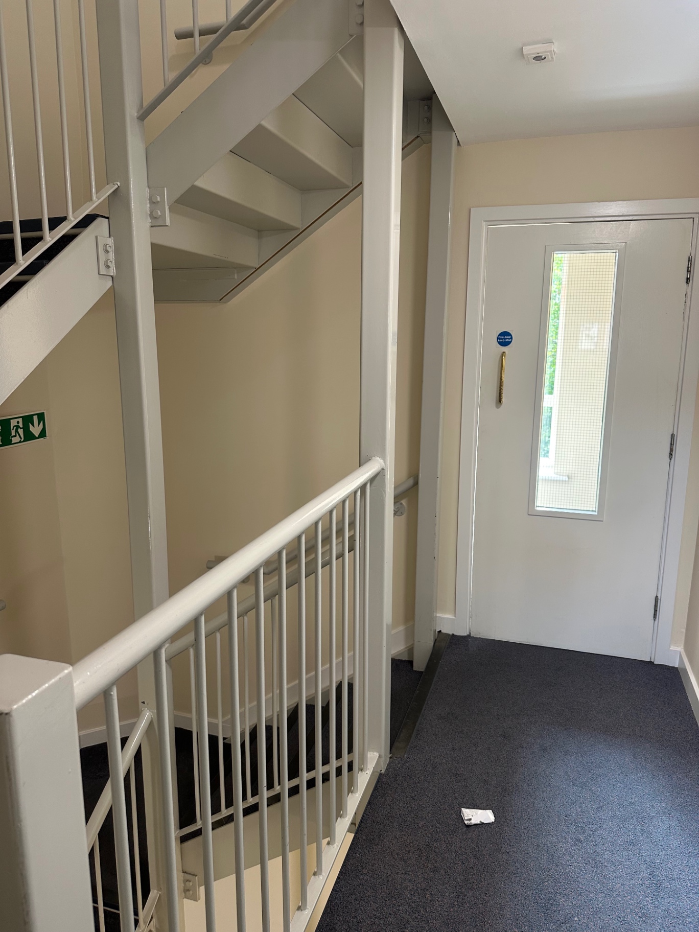 Communal landing with fire door, handrails and freshly painted walls in an occupied apartment block