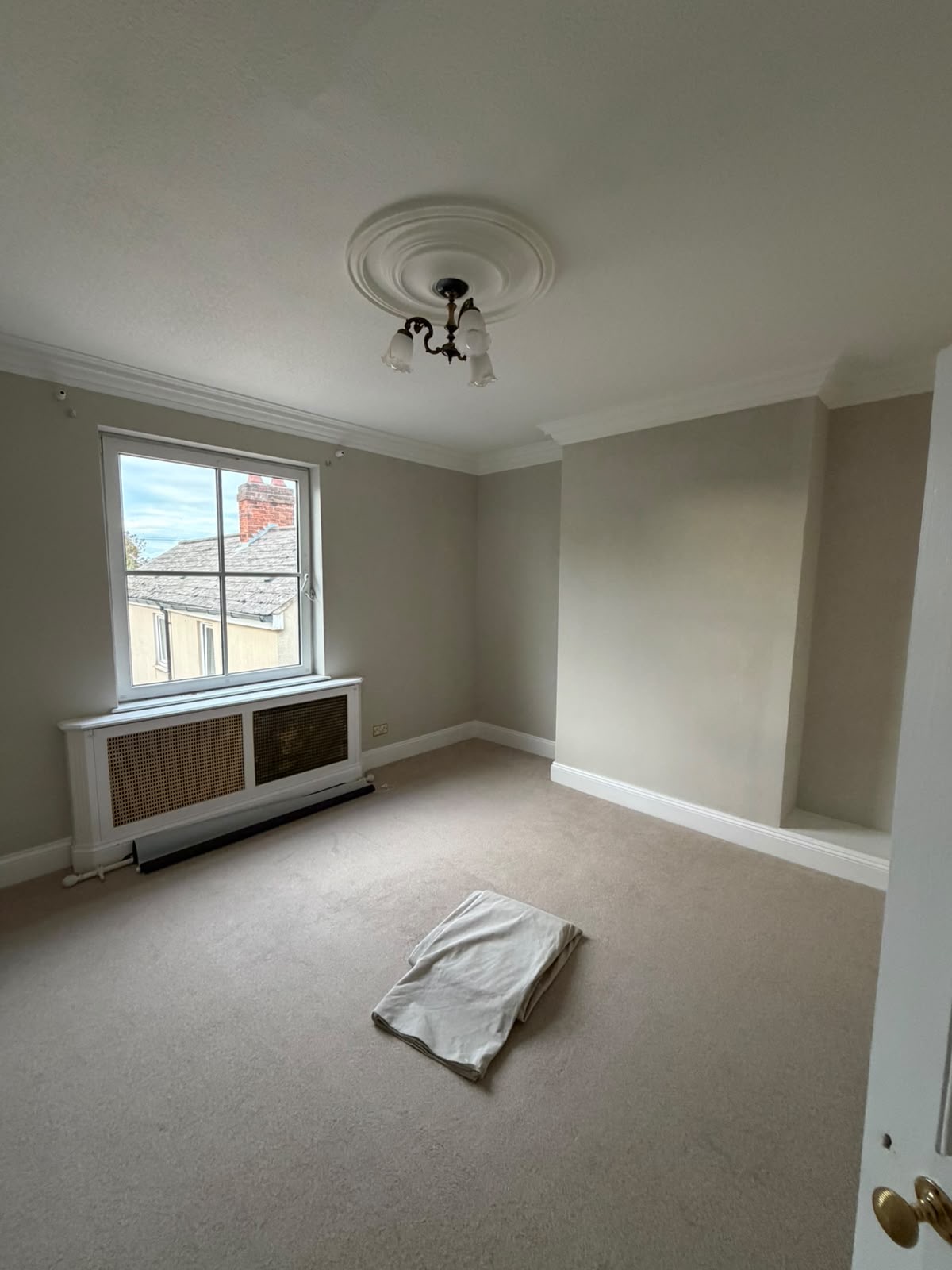 Bedroom with neutral decorated walls, white skirting boards, ceiling rose and window surround above a radiator cover