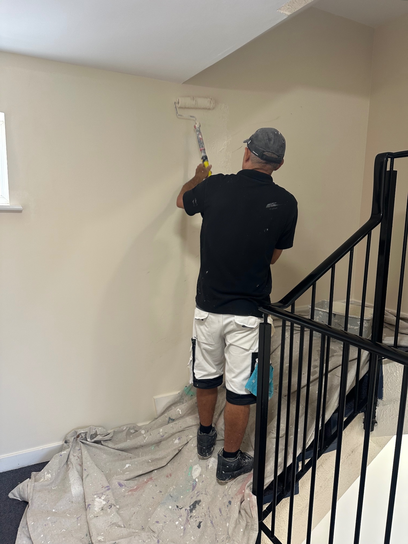 Painter rolling second coat on communal stairwell walls in occupied apartment block