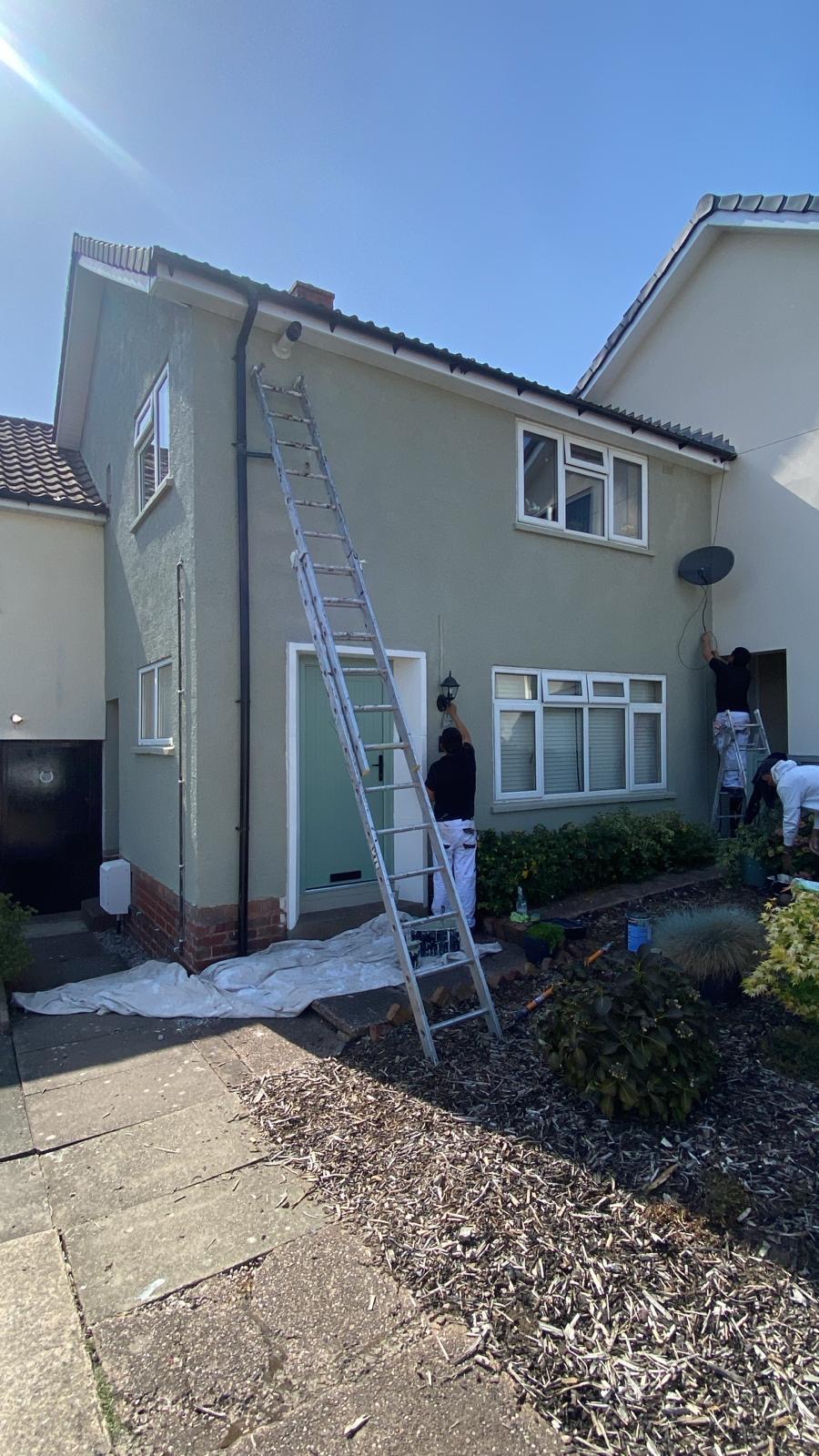 Render Redecoration In Progress Two decorators painting the rendered front elevation of a house from a ladder and step ladder with dust sheets protecting the path