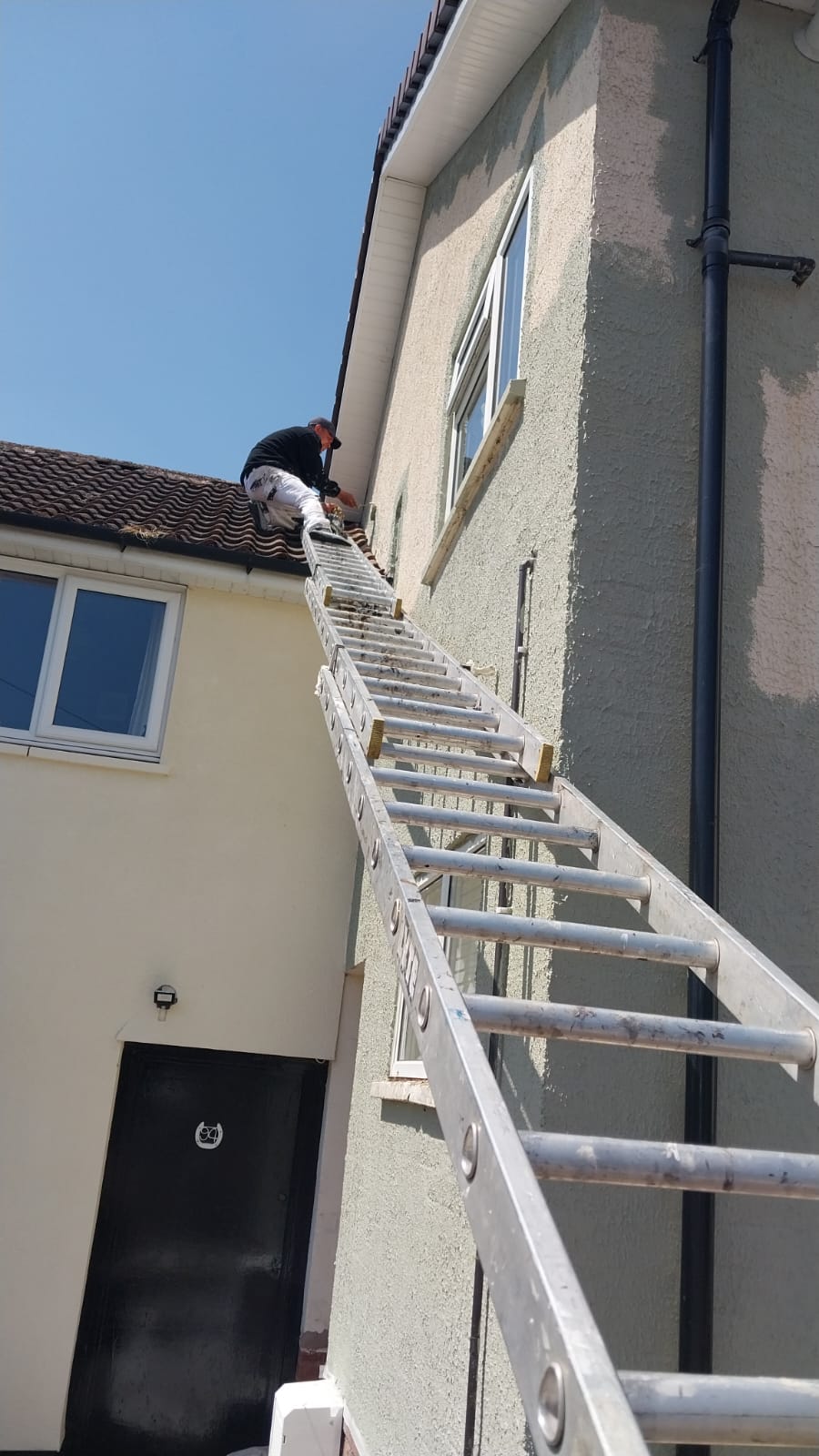 Soffit, Fascia & Render Prep Decorator on a ladder painting a white soffit and fascia above part-primed grey render on a two-storey house