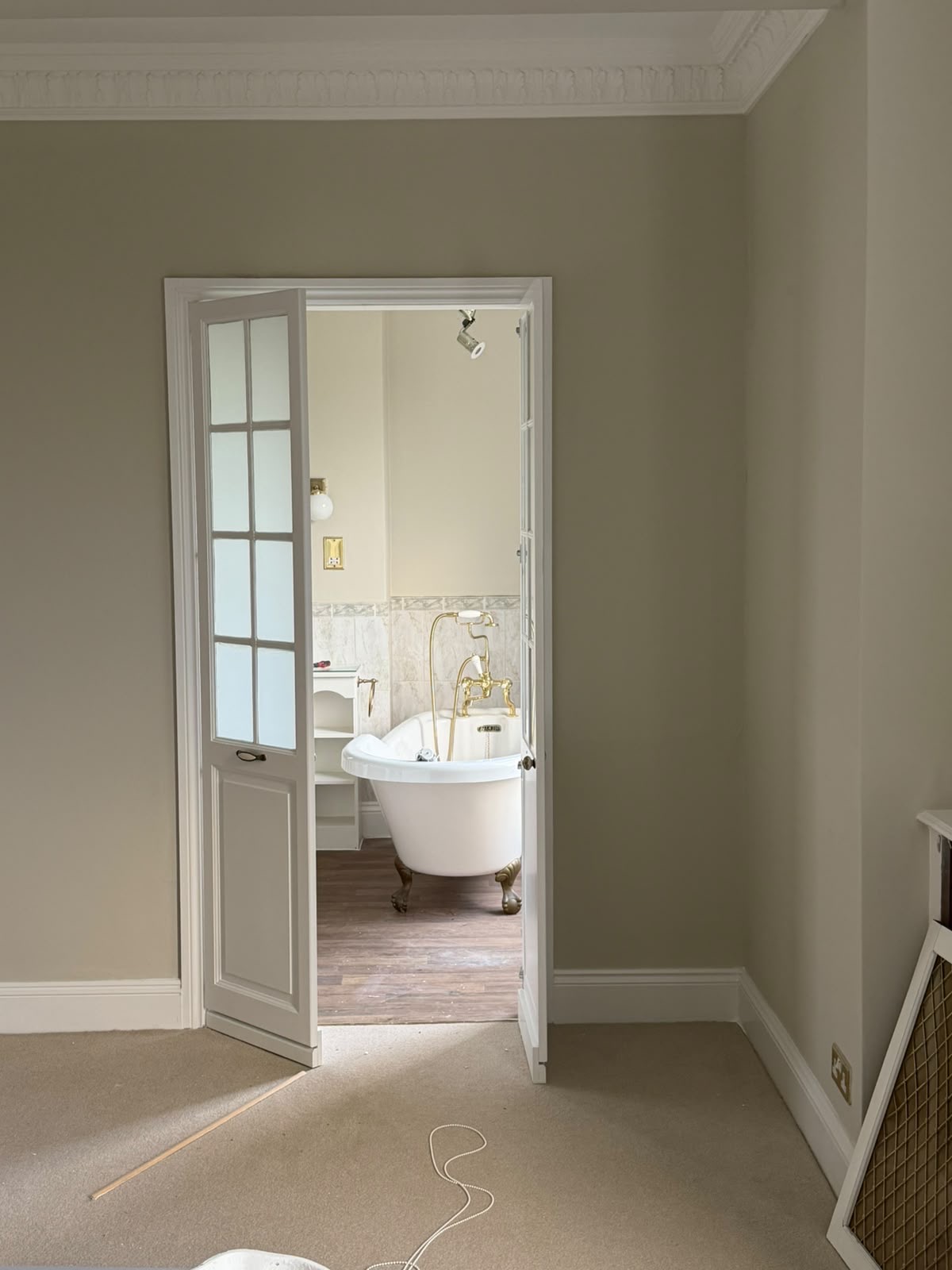White glazed panelled doorway leading from a neutral decorated bedroom to a bathroom with a freestanding bath