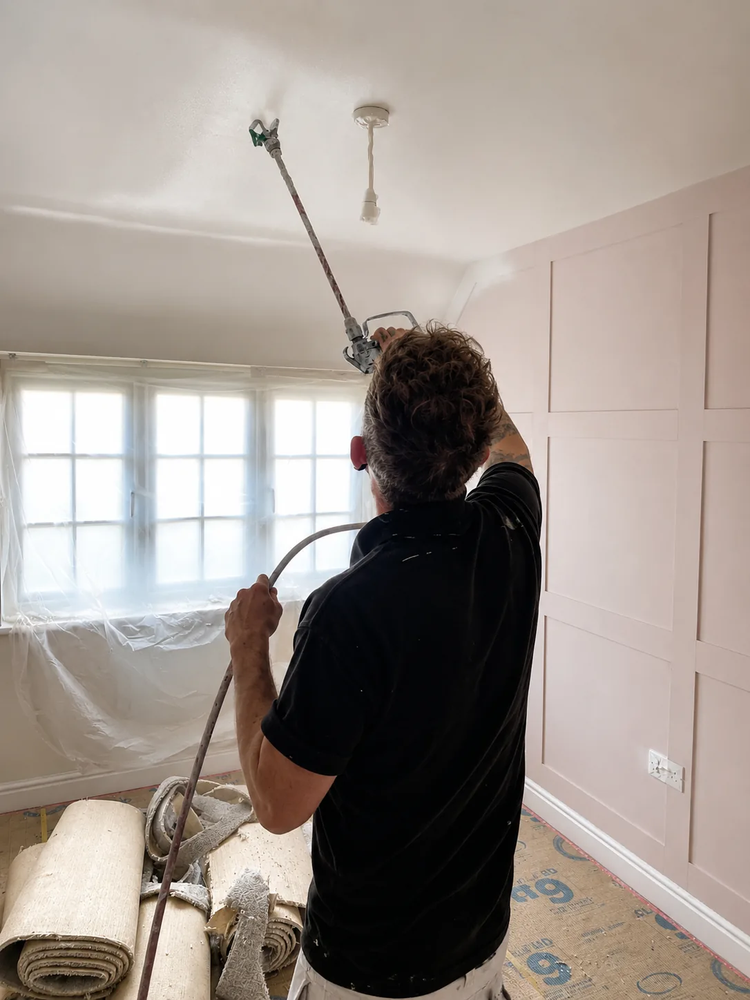 Decorator spraying a ceiling with a Graco airless sprayer and extension pole